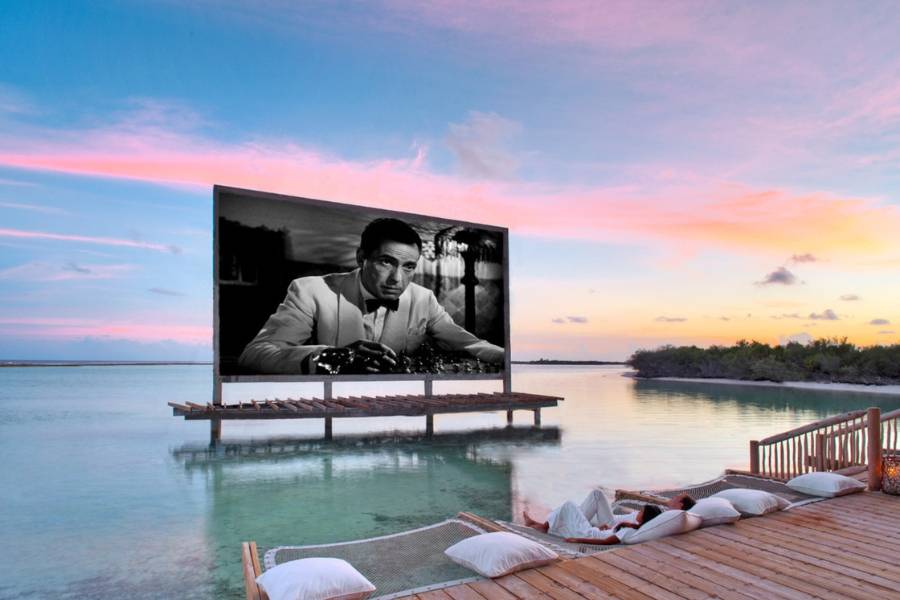 Kinoleinwand über die Lagune in Soneva Jani mit Liegenetzen und weißen Kissen vor einen rosafarbenen Abendhimmel. 