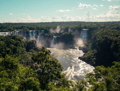 Panoramablick auf die Iguazú-Wasserfälle im tropischen Regenwald mit Boot auf dem Fluss – Naturwunder an der Grenze zwischen Brasilien und Argentinien.