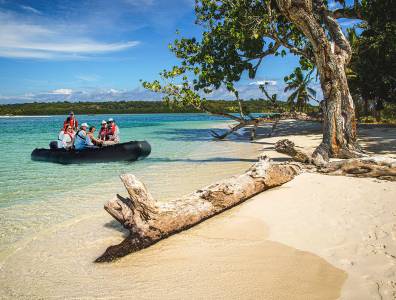 Expeditionsteilnehmer erreichen mit einem Zodiacboot einen tropischen Strand mit Palmen und türkisfarbenem Wasser