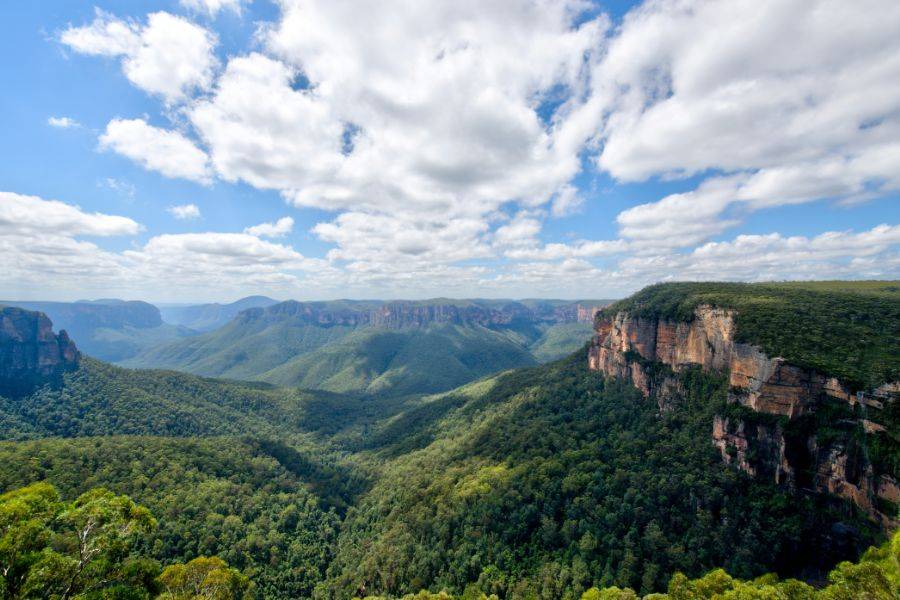 © Unsplash Weitläufiges Panorama der Blue Mountains mit grün bewaldeten Tälern und Sandsteinfelsen unter blauem Himmel mit Wolken