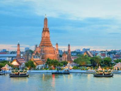 Wat Arun Tempel in Bangkok bei Sonnenuntergang mit beleuchteten Booten auf dem Chao-Phraya-Fluss
