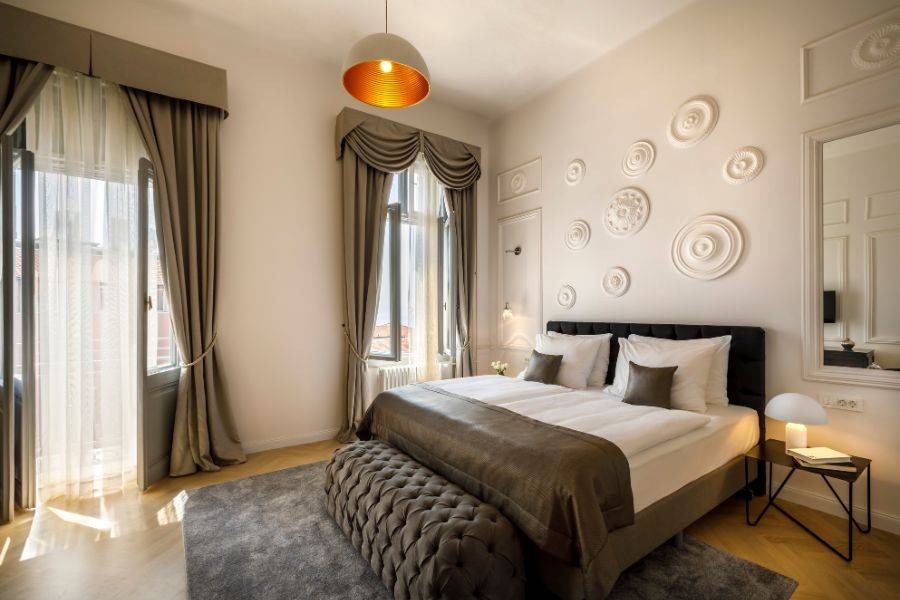 Elegantes Hotelzimmer mit einem großen Bett, neutralen Farben, dekorativen Wandornamenten, einem Schreibtisch und einem Fenster mit Ausblick auf eine grüne Landschaft.