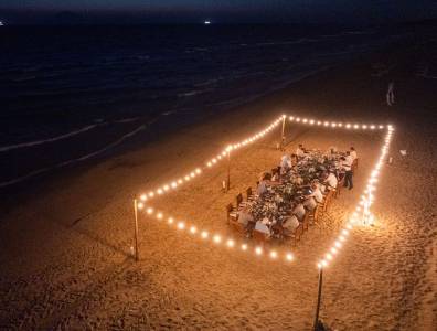 Festlich gedeckte Hochzeitstafel am Strand von Griechenland, umrahmt von Lichterketten, Gäste genießen das Dinner bei Nacht mit Meeresrauschen im Hintergrund.