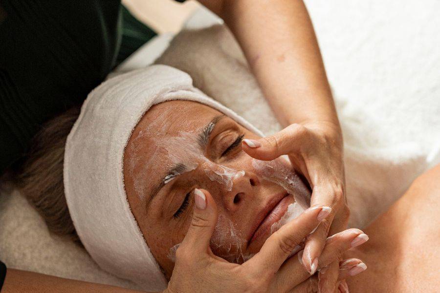 Eine Frau genießt eine entspannende Gesichtsbehandlung, während eine Kosmetikerin sanft eine Gesichtsmaske aufträgt.