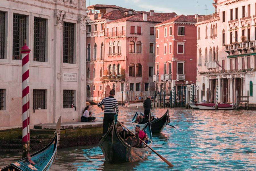 Gondeln mit Passagieren gleiten durch einen kleinen Kanal in Venedig, umgeben von historischen Gebäuden mit typischer venezianischer Architektur.