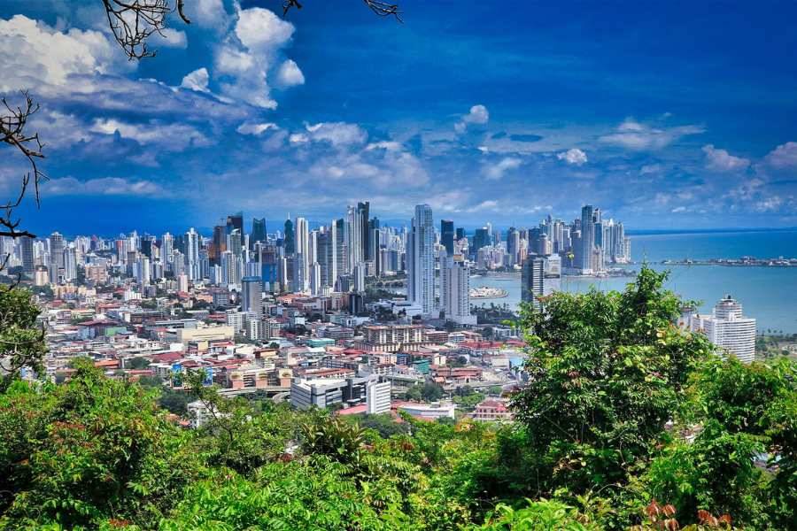 Blick auf die Skyline von Panama-Stadt mit zahlreichen Hochhäusern, umgeben von tropischem Grün und Küste.