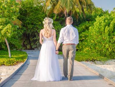 Braut und Bräutigam gehen Hand in Hand auf einem Holzweg durch tropische Landschaft auf den Malediven.