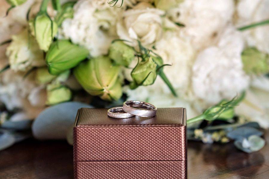 Zwei Eheringe liegen auf einer Ringschachtel. Um sie herum liegt Blumenschmuck.