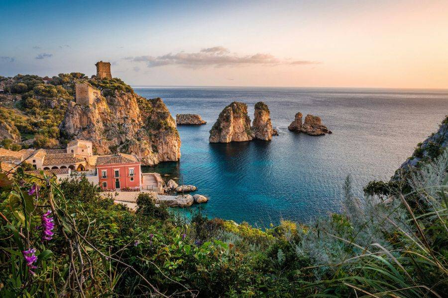 Malerische Küstenlandschaft mit steilen Felsen, türkisfarbenem Wasser und historischen Gebäuden bei Sonnenuntergang, Blick auf das Meer.