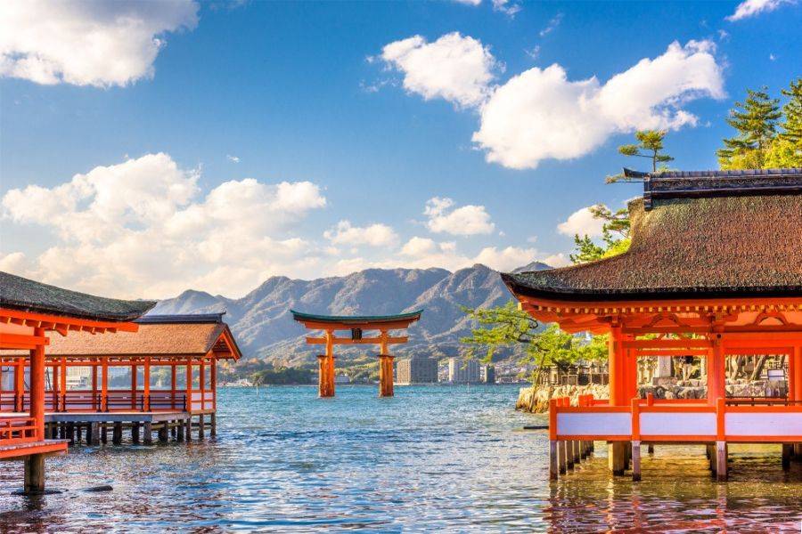 Schwimmendes Torii des Itsukushima-Schreins in Hiroshima mit traditionellen Gebäuden, Meer und Bergen im Hintergrund