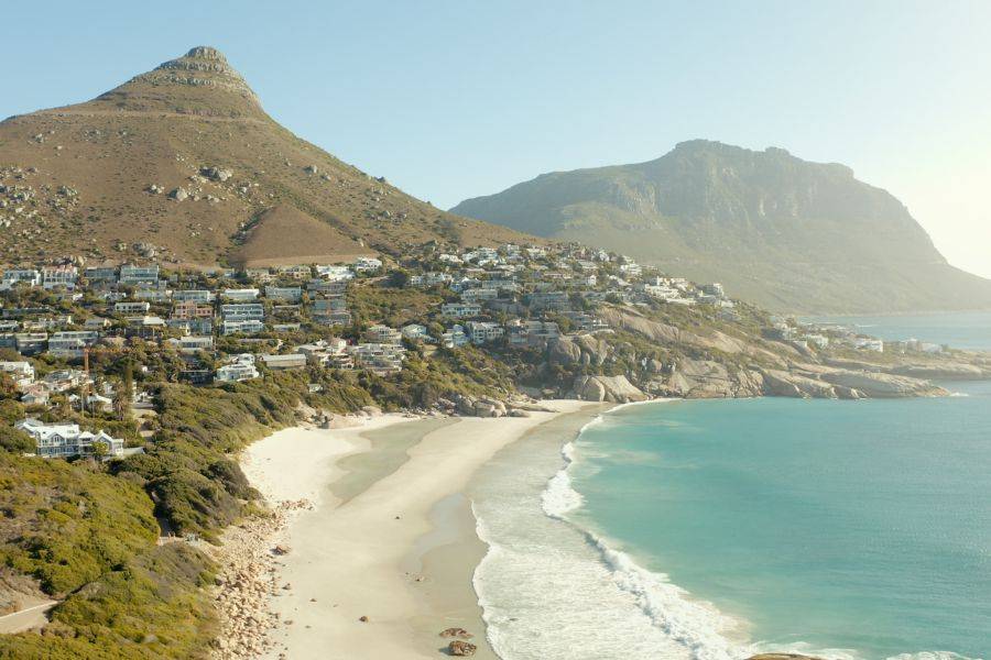 Ruhiger Strand am Fuße einer bergigen Landschaft mit Häusern an den Hängen, die sich entlang der Küste erstrecken.