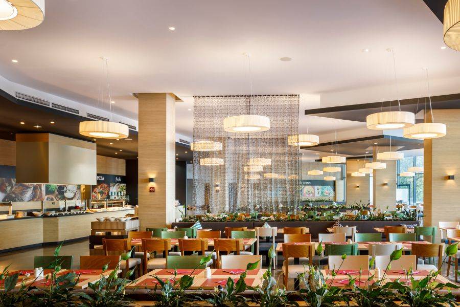 Großzügiges, modernes Restaurant mit Panoramafenstern, die einen Blick auf das Meer und die Bäume bieten, stilvollen Möbeln und eleganter Beleuchtung.