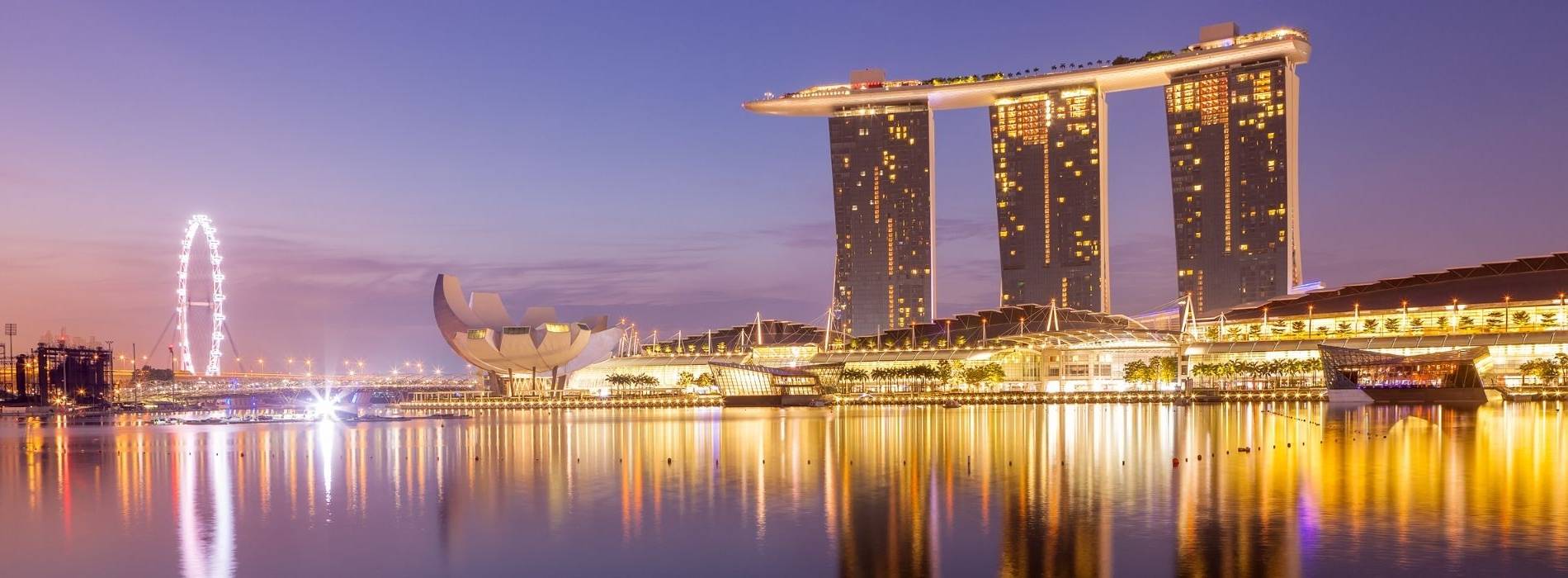 Skyline von Singapur bei Nacht mit Marina Bay Sands und beleuchtetem Riesenrad am Wasser