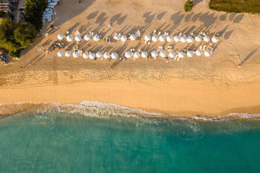 Lutaufnahme eines Sandstrands mit weißen Sonnenschirmen und türkisblauem Meer