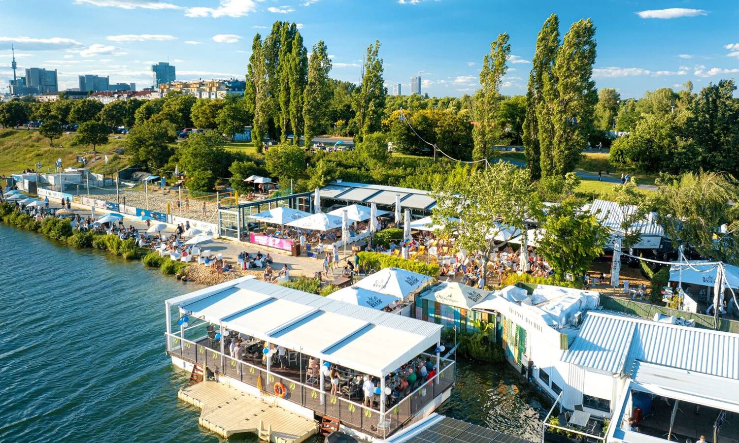 Luftaufnahme des Vienna City Beach Club mit Strand, Volleyballfeldern und Lounges am Wasser