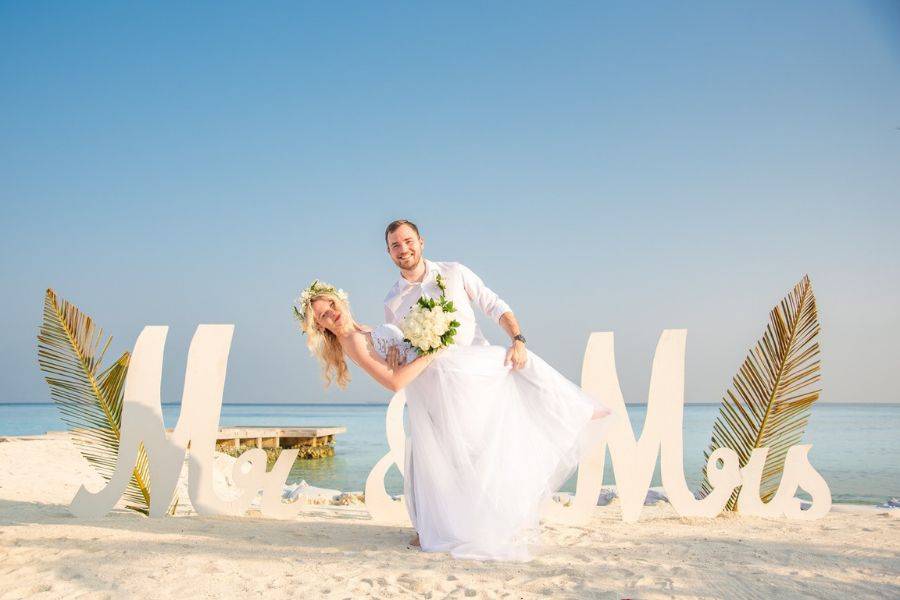 Brautpaar bei einer romantischen Strandhochzeit auf den Malediven vor „Mr & Mrs“ Schriftzug.