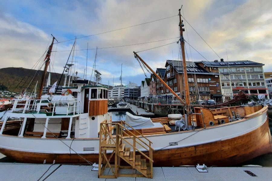 Ein traditionelles Holzboot in einem Hafen, umgeben von historischen Gebäuden und einer malerischen Kulisse, mit ruhigem Wasser und bewölktem Himmel.