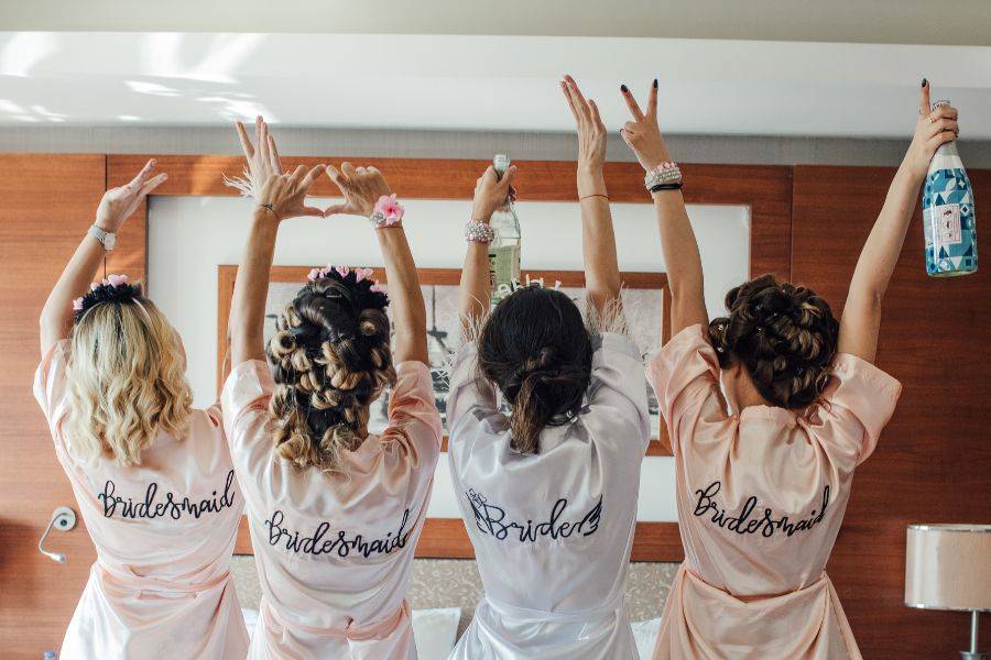 Vier Frauen sitzen von einem Bett. Jede von ihnen trägt einen Bademantel, der hinten mit 