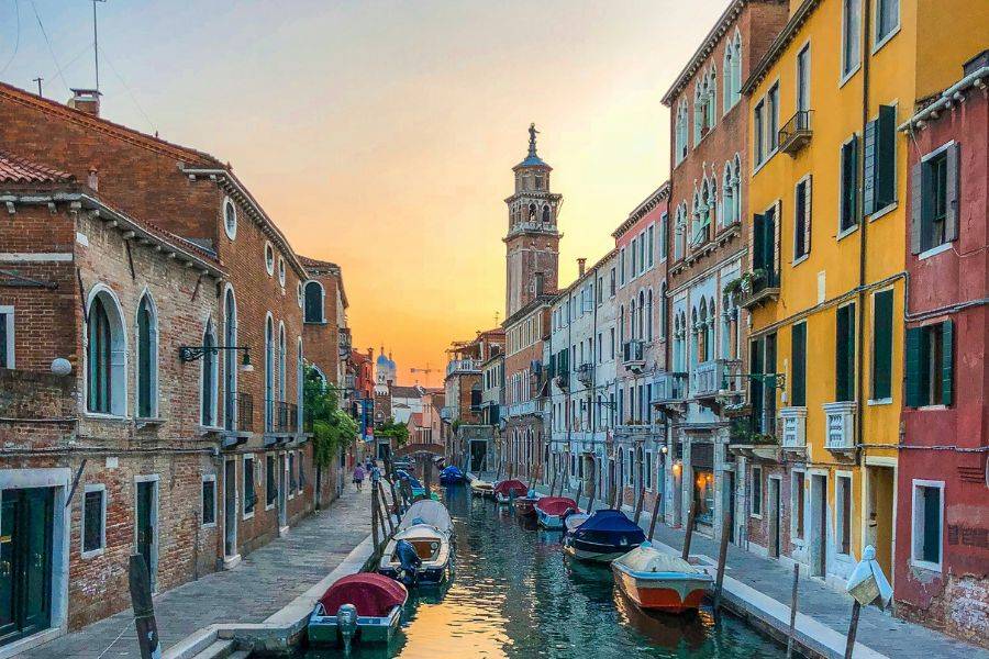 Romantischer Blick auf einen Seitenkanal in Venedig mit bunten Häuserfassaden und Booten bei warmem Abendlicht.