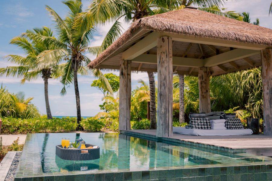 Blick auf eine der privaten Infinity-Pools mit Floating Breakfast. Dahinter sieht man Palmen.
