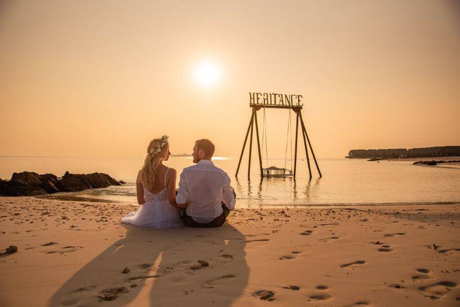 Brautpaar sitzt bei Sonnenuntergang am Strand der Malediven und genießt romantische Flitterwochen.