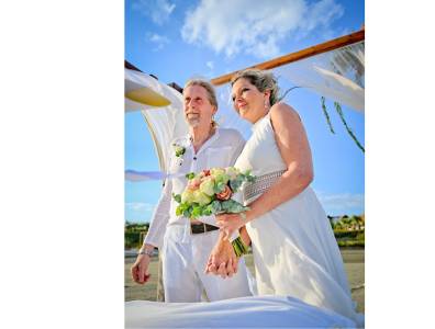 trandhochzeit auf Zypern: Brautpaar unter einem Hochzeitsbogen mit Blumenschmuck, in festlicher weißer Kleidung und mit Brautstrauß – Heiraten im Ausland bei Sonnenschein.