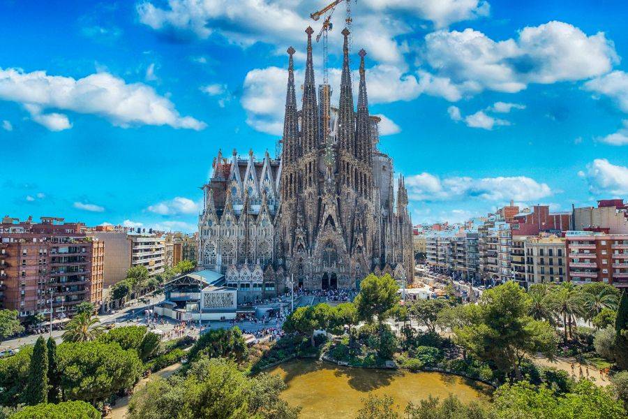 Die weltberühmte Basilika von Antoni Gaudí mit ihren hoch aufragenden Türmen und detailreichen Fassaden, vor einem strahlend blauen Himmel.