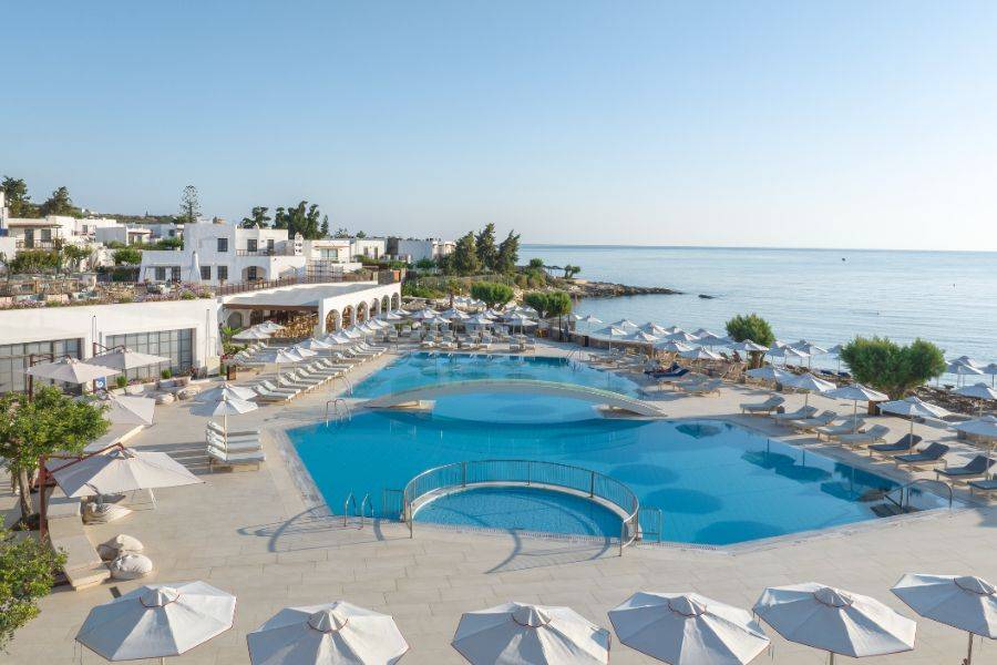 Blick auf die weitläufige Poollandschaft des Creta Maris Beach Resorts direkt am Meer mit weißen Sonnenschirmen und mediterranem Flair.