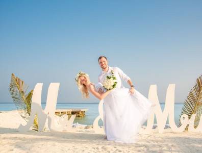 Brautpaar bei einer romantischen Strandhochzeit auf den Malediven vor „Mr & Mrs“ Schriftzug.