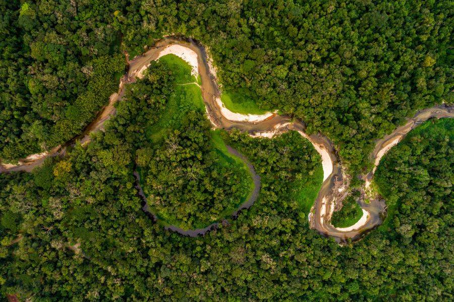 Luftaufnahme eines sich windenden Flusses, der sich durch den dichten, grünen Amazonas-Regenwald in Peru schlängelt.