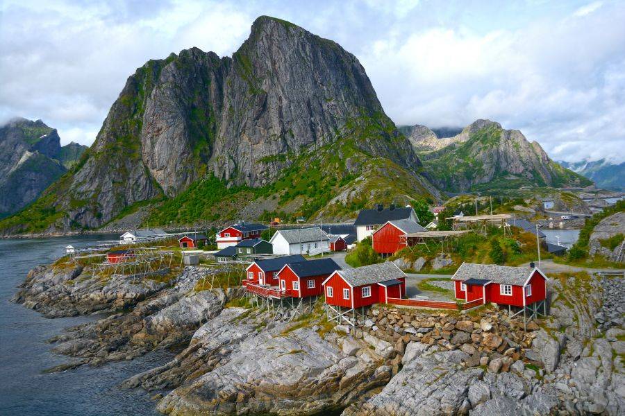 Rote Fischerhütten auf den Lofoten vor steilen Bergen und fjordreicher Küstenlandschaft in Norwegen