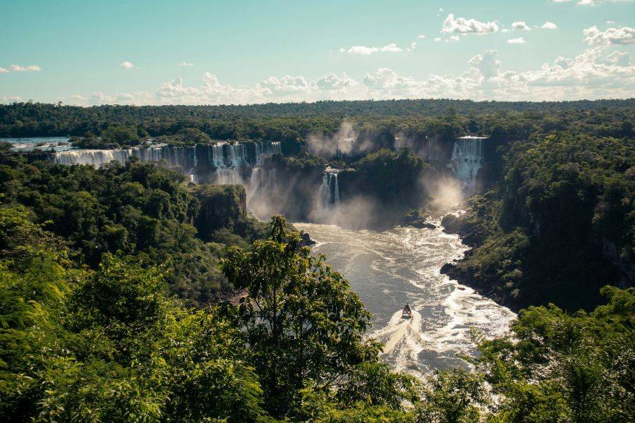 Panoramablick auf die Iguazú-Wasserfälle im tropischen Regenwald mit Boot auf dem Fluss – Naturwunder an der Grenze zwischen Brasilien und Argentinien.