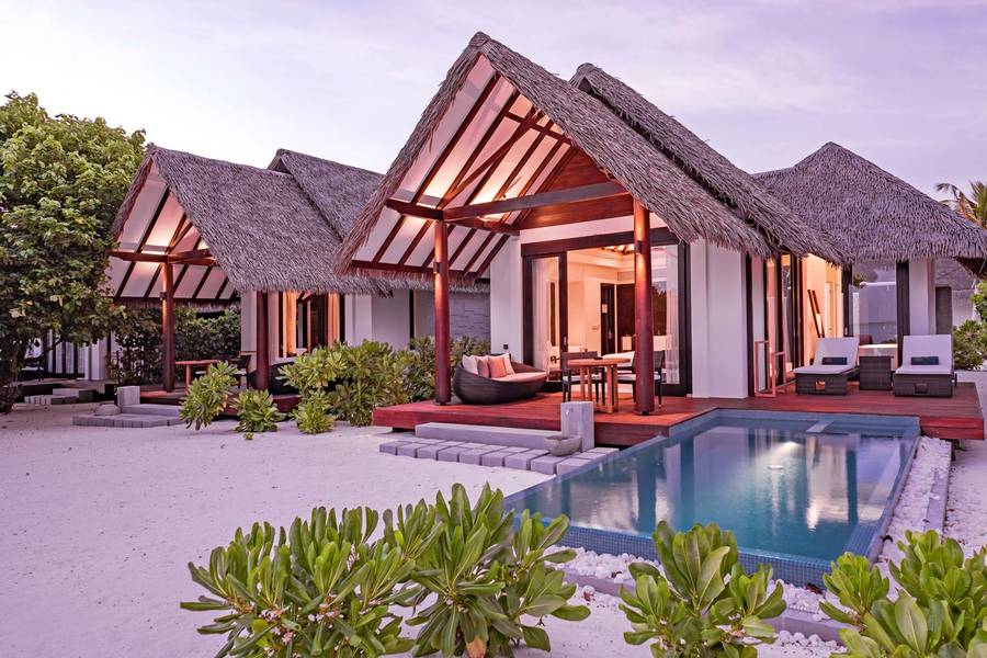 Strandvilla mit traditionellem Strohdach, privatem Pool, Holzterrasse und umgeben von tropischem Grün, direkt am weißen Sandstrand.