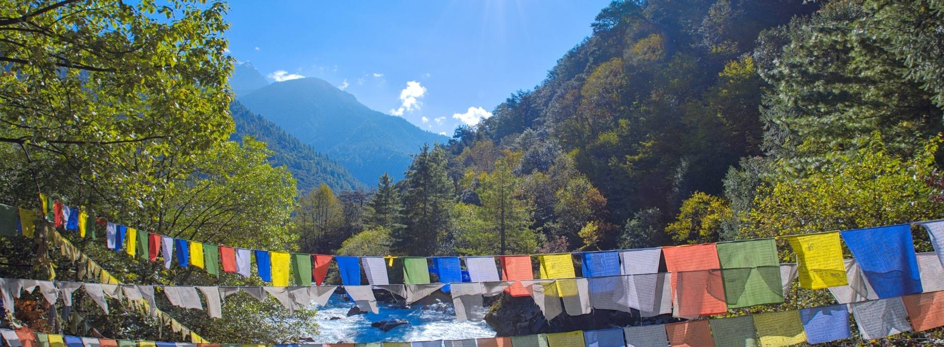 Bunte Gebetsfahnen über einem Fluss in bergiger Landschaft im Himalaya, Bhutan