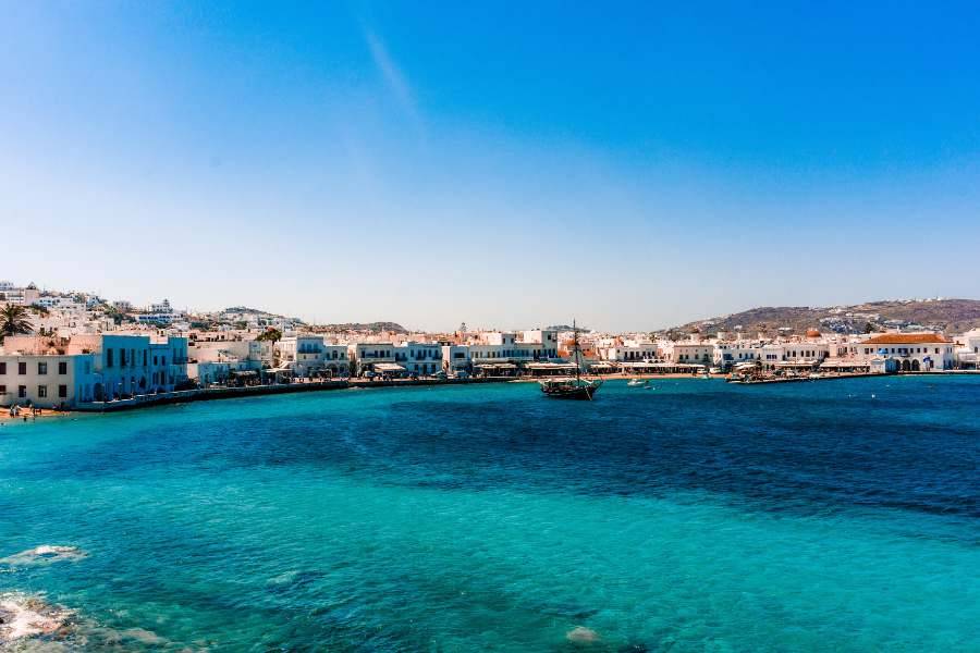 Klares türkisfarbenes Meer vor einer Küstenstadt mit typisch weiß-blauer Architektur.