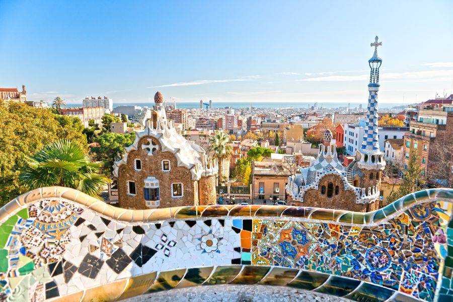  Die verspielte Architektur von Gaudí mit bunten Mosaikfliesen, geschwungenen Formen und einem Panorama über die Stadt Barcelona bis zum Meer.