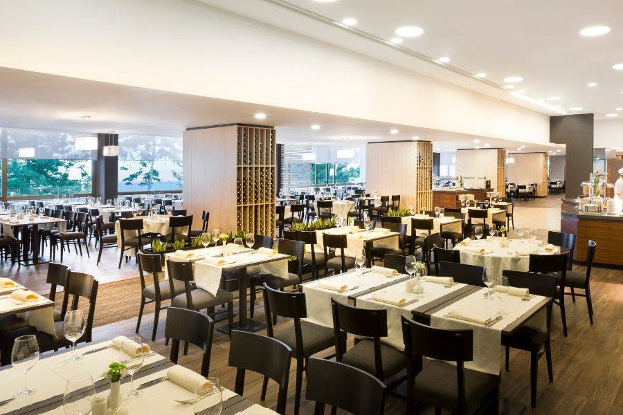 Modernes Restaurant mit stilvoll gedeckten Tischen, einer offenen Küche, Wanddekorationen und einem farbenfrohen Gemälde als Blickfang.