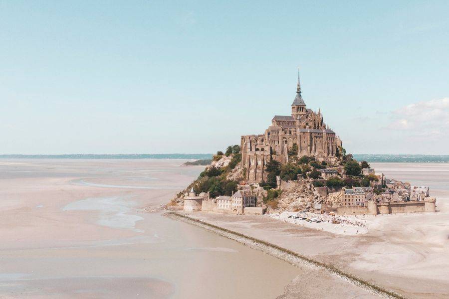Das Kloster Mont-Saint-Michel erhebt sich majestätisch aus dem Wattenmeer bei Ebbe, umgeben von Sandflächen und weitem Horizont.