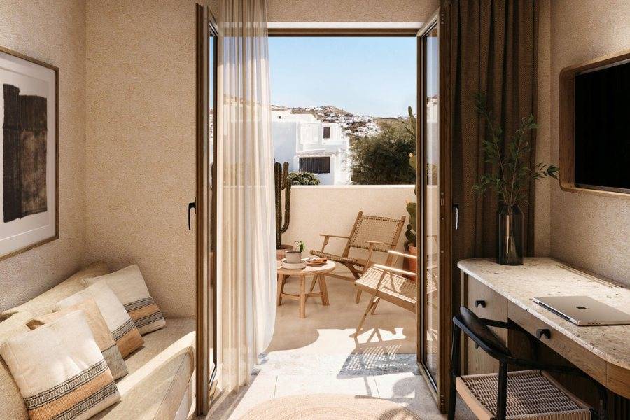 Helles Hotelzimmer mit Balkon, auf dem zwei Holzstühle und ein Tisch stehen.