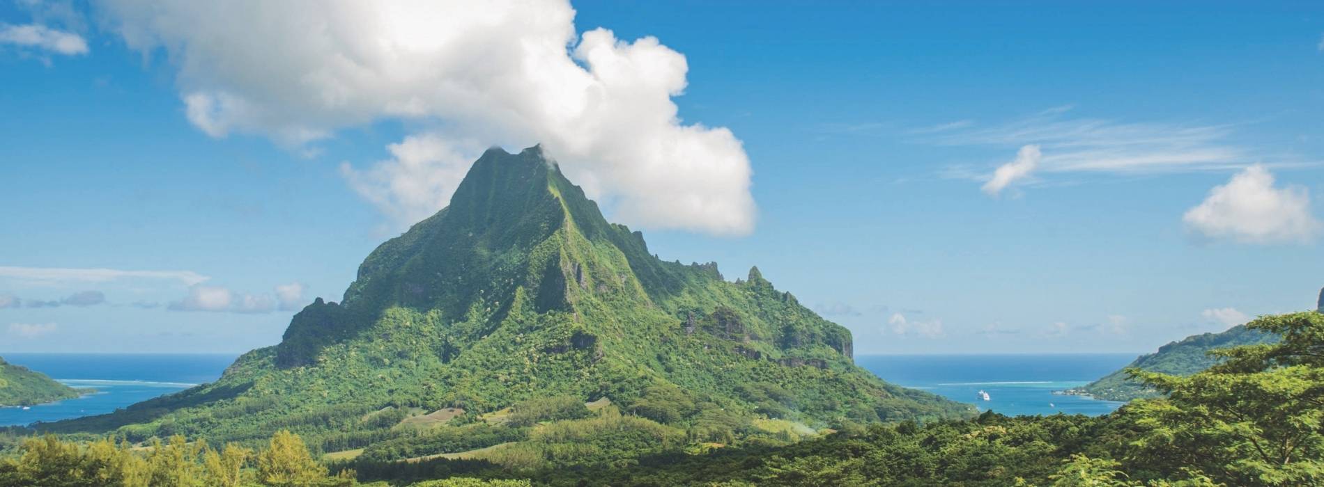Grüne Vulkaninsel mit markantem Bergmassiv, üppischer Vegetation und Blick auf das tiefblaue Meer unter leicht bewölktem Himmel