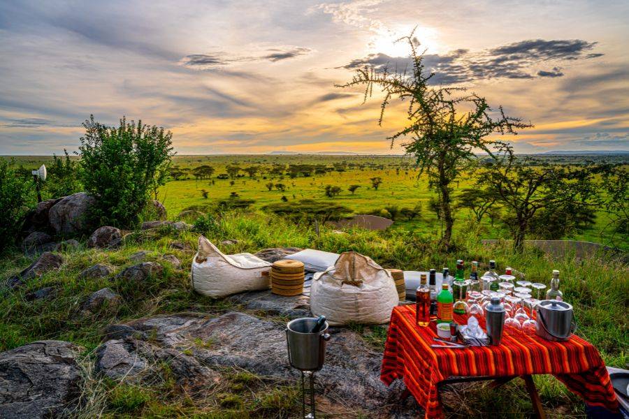 Ein Picknick in der Serangeti. Im Hintergrund sieht man wie der Sonnenuntergang den Himmel in ein Orange färbt.