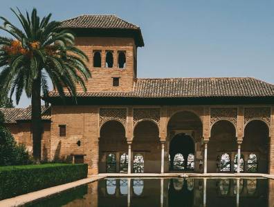 Dieses Bild zeigt die Alhambra in Granada, eines der beeindruckendsten Beispiele maurischer Architektur in Spanien. Die filigranen Bögen, die warmen Erdtöne der Backsteine und die Spiegelung im Wasserbecken verleihen der Szene eine fast märchenhafte Atmosphäre.