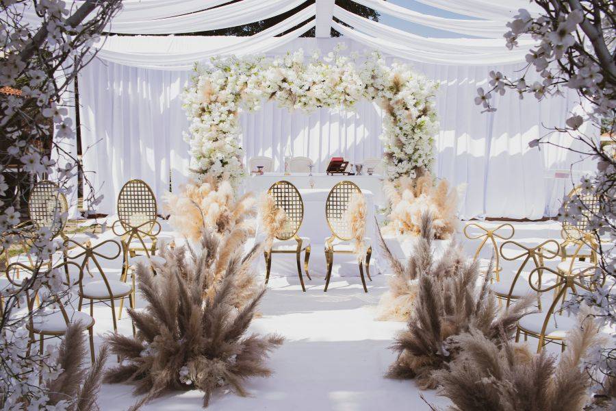 Romantisch dekorierte Hochzeitskulisse im Freien mit weißen Vorhängen, floralen Elementen und eleganter Bestuhlung unter einem Zeltdach.