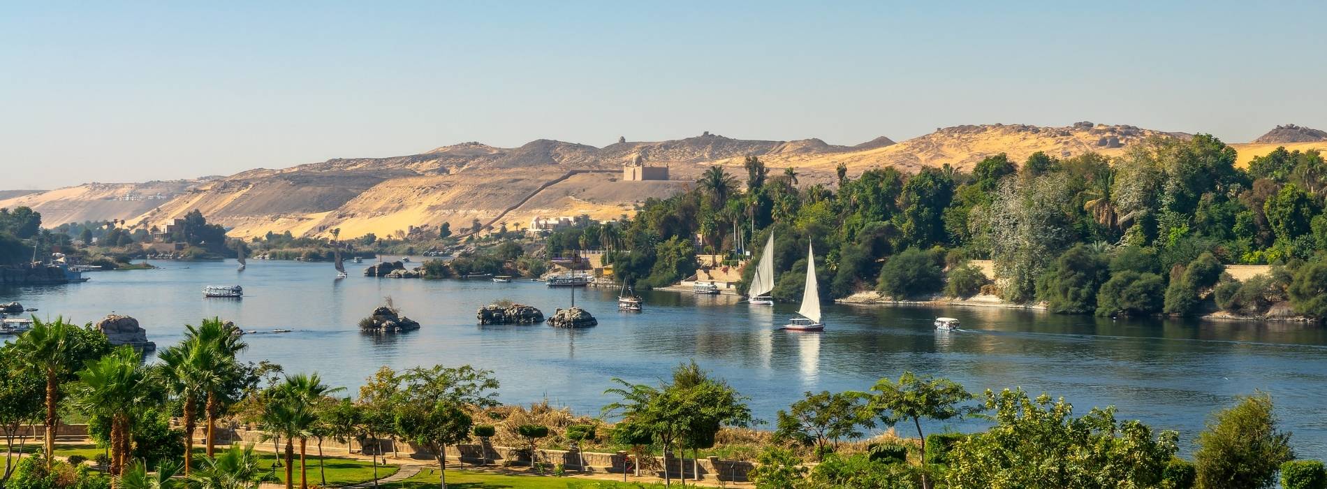 Nilufer mit Booten und grünen Inseln bei Assuan, Ägypten, mit Wüstenhügeln im Hintergrund