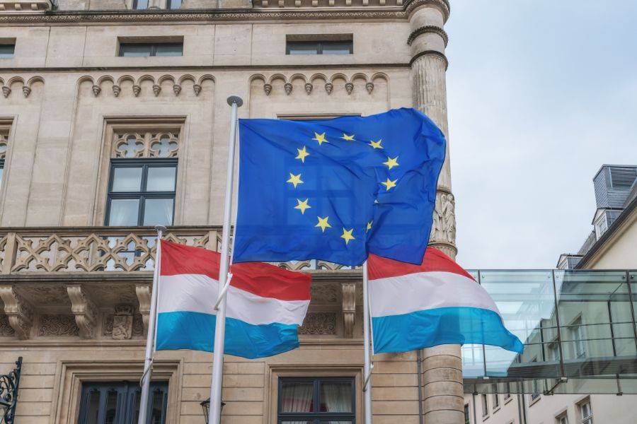 Luxemburgische und europäische Flaggen wehen vor einem historischen Gebäude in Luxemburg-Stadt – Symbol für die europäische Verbundenheit des Landes.