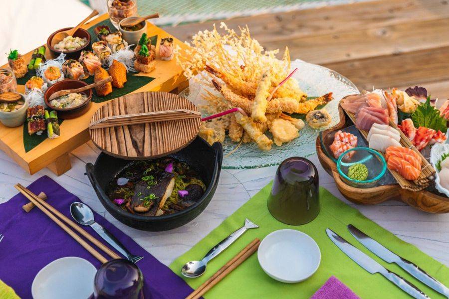 Sushi, Sashimi und Tempura auf einem gedeckten Tisch mit bunten Platzsets im Soneva Jani. 