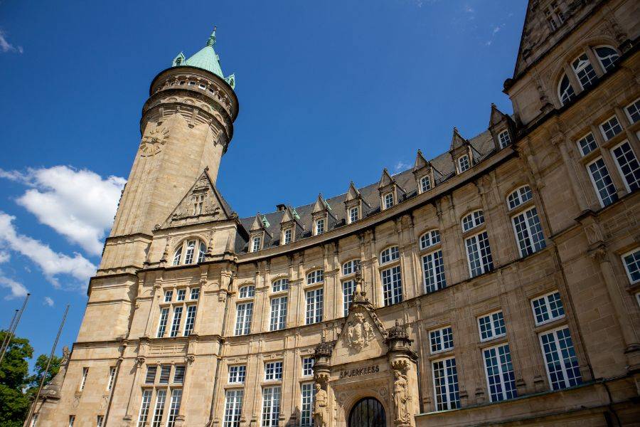 Ansicht der historischen Banque et Caisse d'Épargne de l'État in Luxemburg-Stadt mit markantem Rundturm und blauer Kuppel bei klarem Himmel.