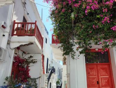 Romantische Gasse auf Mykonos mit blühender Bougainvillea und traditionellen weiß-roten Häuserfassaden.
