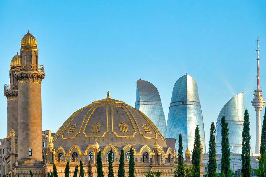 Im Vordergrund steht eine prachtvolle Moschee mit einer goldenen Kuppel und einem kunstvoll gestalteten Minarett, das die historische und religiöse Bedeutung des Landes unterstreicht. Im Hintergrund erheben sich die ikonischen Flame Towers, die mit ihrer modernen, futuristischen Architektur das Stadtbild prägen.