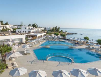 Blick auf die weitläufige Poollandschaft des Creta Maris Beach Resorts direkt am Meer mit weißen Sonnenschirmen und mediterranem Flair.